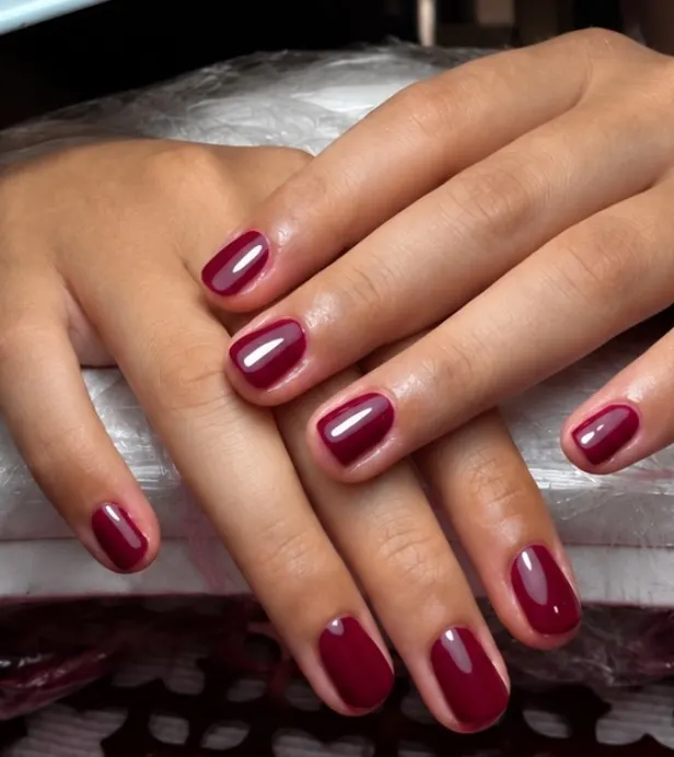 Mani con smalto bordeaux lucido appoggiate sul cuscino da manicure del centro