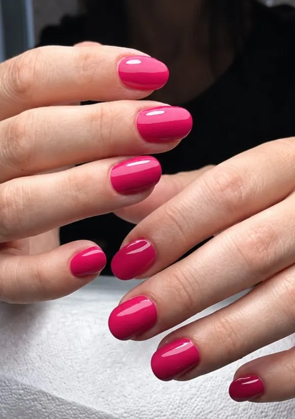 Mani con smalto fucsia, unghie corte e arrotondate, sul cuscino da manicure